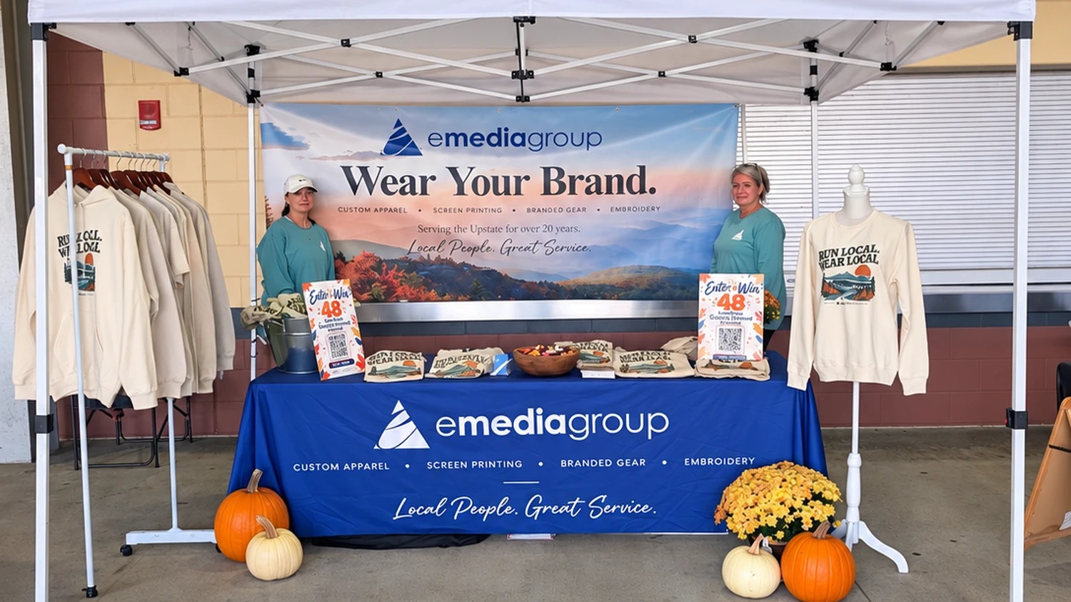 emediagroup promotional booth at Spinx Run Fest 2026 expo at Fluor Field featuring custom screen printed apparel, event banners, and Run Local Wear Local shirts
